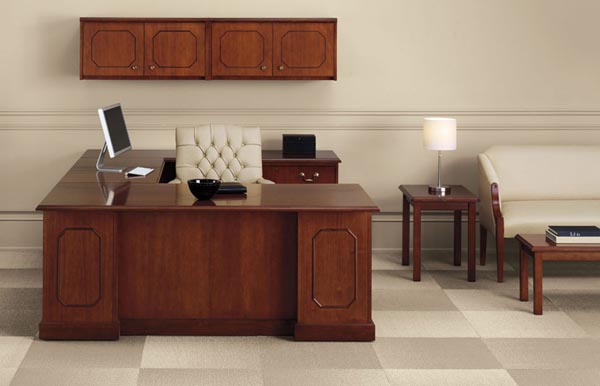 Executive traditional "U" desk consisting of a single pedestal desk, bridge, single pedestal credenza with overhead storage with doors. To the right is a sitting area consisting of an end table, sofa and coffee table.
